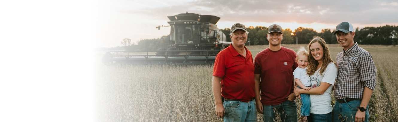 Three generations of a farming family standing in a field in front of a combine.